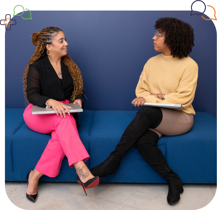 Woman in black shirt and pink pants sitting next to another woman with black boots and a yellow sweater on a blue sofa