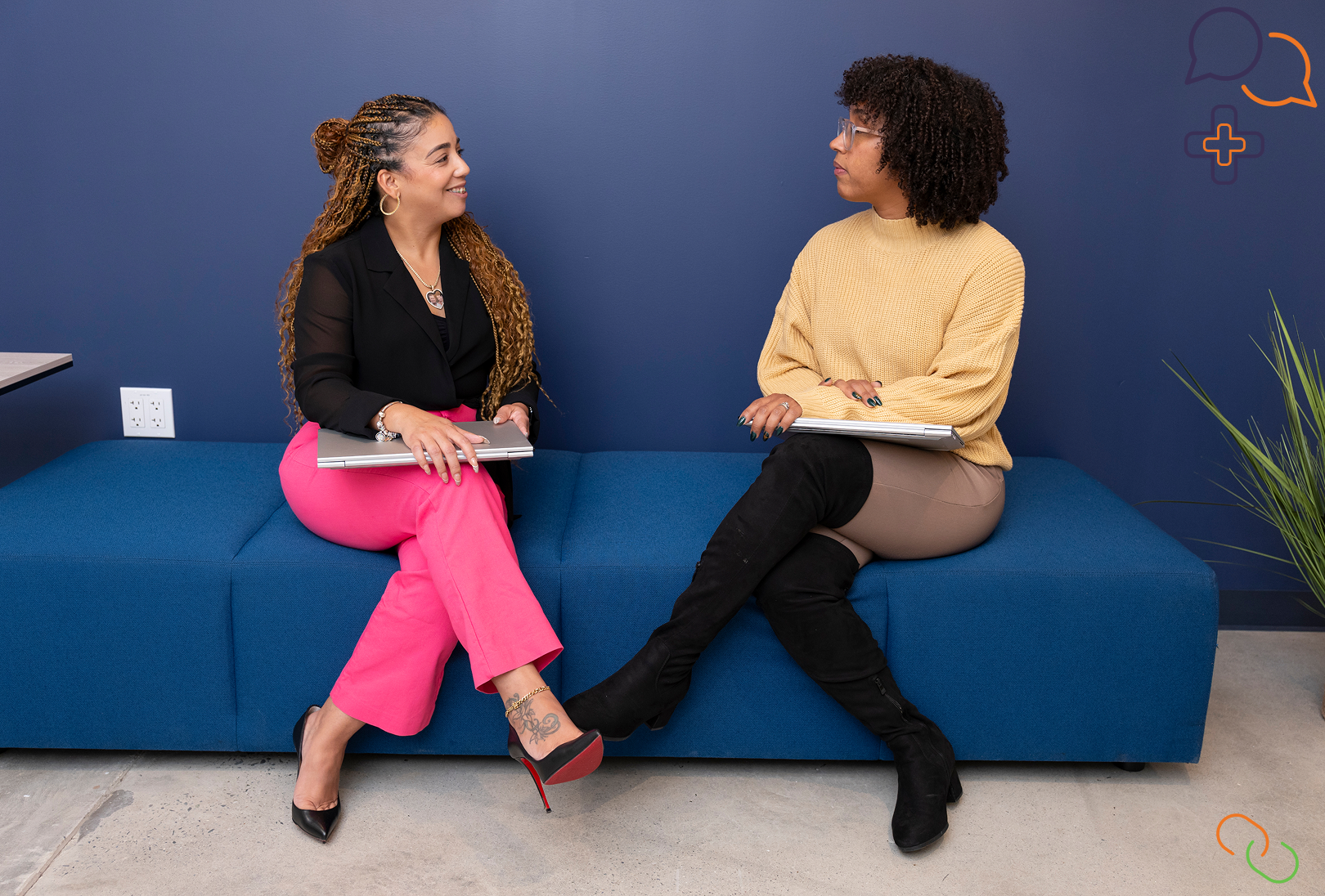 Woman in black shirt and pink pants sitting next to another woman with black boots and a yellow sweater on a blue sofa