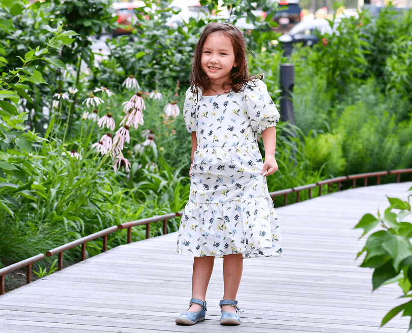 Little girl in a floral dress with blue shoes standing on a deck