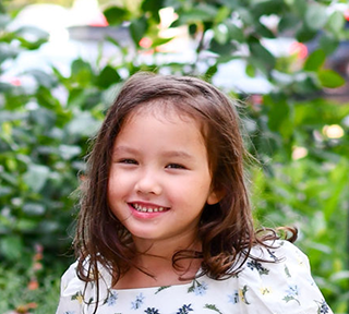 Niña con cabello castaño oscuro con un top floral sonriendo.