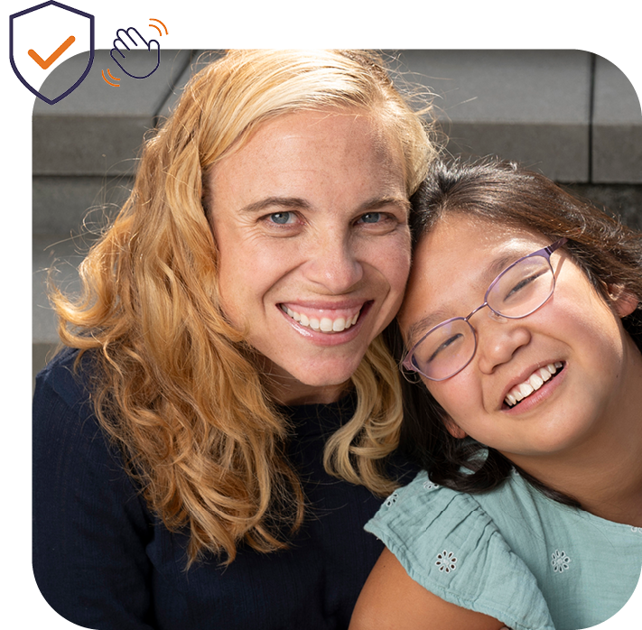 Blond woman in dark sweater and dark hair girl with glasses smiling