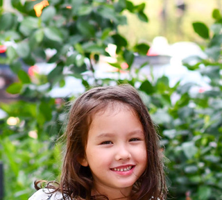 Little girl with dark brown hair in a floral top smiling